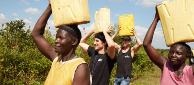 Menschen in Uganda tragen Wasserkästen auf dem Kopf.