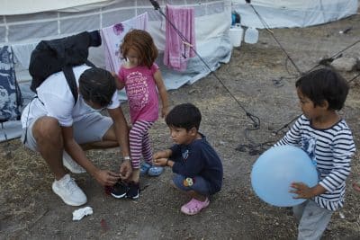 Serkan bindet einem Kind in Griechenland die Schuhe zu.