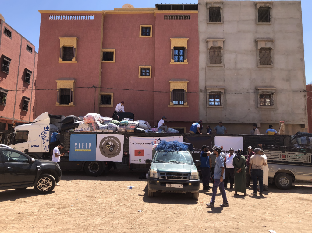 Auf dem Bild ist ein großer LKW mit diversen Hilfsgütern zu sehen. Auf dem LKW ist ein STELP Logo, ein Logo der Organisation Helping Hands Africa sowie ein Logo er Organisation al Ofoq Charity Association zu sehen.