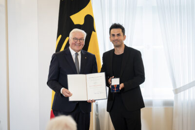 STELP-Gründer SErkan Eren erhält von Frank Walter Steinmeier persönlich sein Bundesverdienstkreuz. Sie lächeln beide in die Kamera.