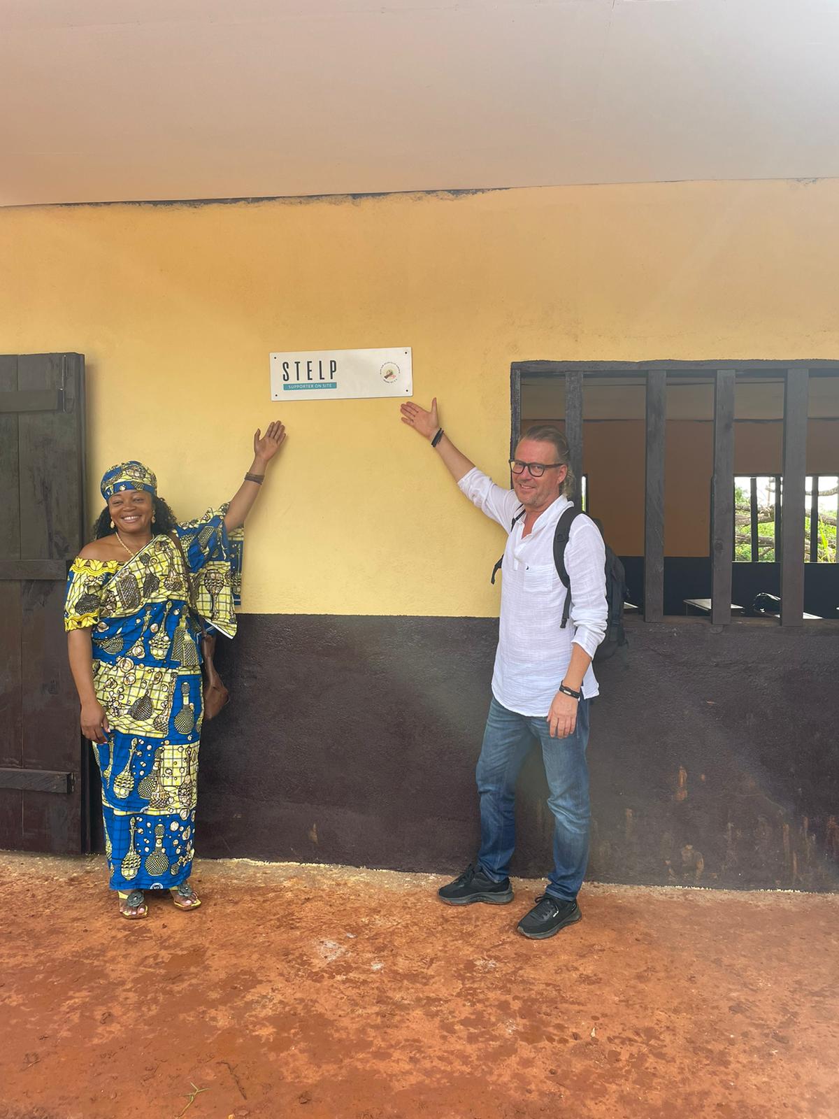 Schuleröffnung in Kamerun. Eine Frau und ein Mann zeigen auf das Eröffnungschild.