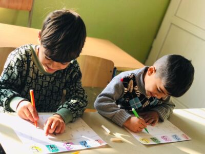 Zwei Schüler aus dem Irak basteln an ihren Kunstwerken und lächeln dabei.